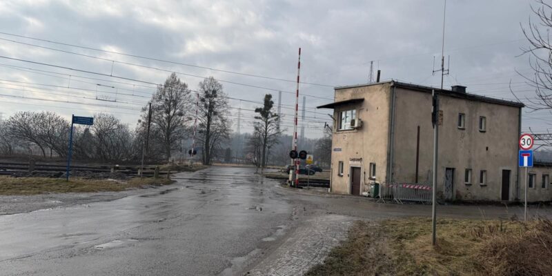 Zimowy widok na ul. Nadwiślańską w Oświęcimiu (Dwory) prowadzącą w stronę przejazdu kolejowego. Droga jest częściowo oblodzona i pokryta śniegiem, po prawej stronie widać tory oraz infrastrukturę kolejową, a w oddali świecą czerwone światła sygnalizacji.