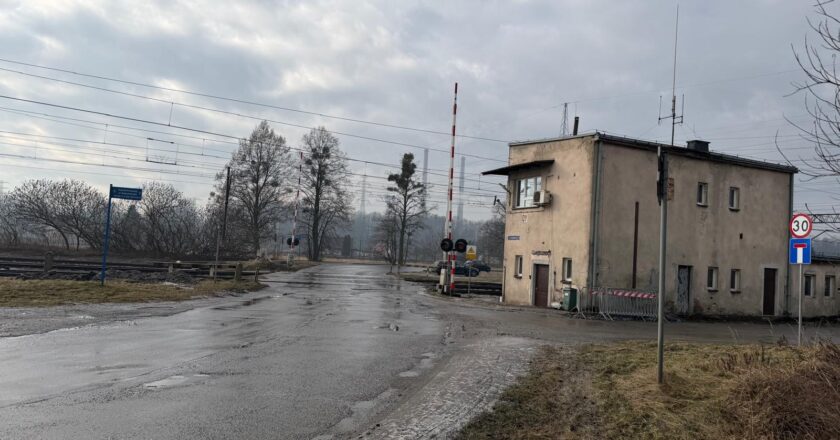 Zimowy widok na ul. Nadwiślańską w Oświęcimiu (Dwory) prowadzącą w stronę przejazdu kolejowego. Droga jest częściowo oblodzona i pokryta śniegiem, po prawej stronie widać tory oraz infrastrukturę kolejową, a w oddali świecą czerwone światła sygnalizacji.