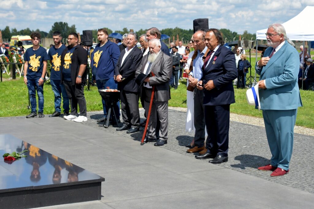 Uczestnicy uroczystości upamiętniającej zagładę Romów i Sinti składają wieniec przy pomniku w byłym obozie Auschwitz II-Birkenau. W tle widoczne namioty, zgromadzeni goście i przedstawiciele władz.