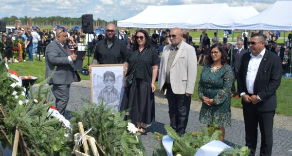 Uczestnicy uroczystości upamiętniającej zagładę Romów i Sinti składają wieniec przy pomniku w byłym obozie Auschwitz II-Birkenau. W tle widoczne namioty, zgromadzeni goście i przedstawiciele władz.