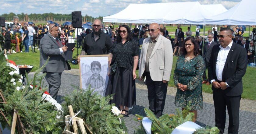 Uczestnicy uroczystości upamiętniającej zagładę Romów i Sinti składają wieniec przy pomniku w byłym obozie Auschwitz II-Birkenau. W tle widoczne namioty, zgromadzeni goście i przedstawiciele władz.