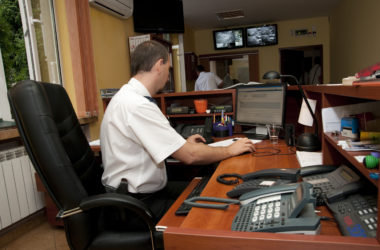 Dyżurny policjant pracujący przy biurku w komendzie, monitorujący sytuację na ekranach komputerów i systemie kamer. Policja Oświęcim
