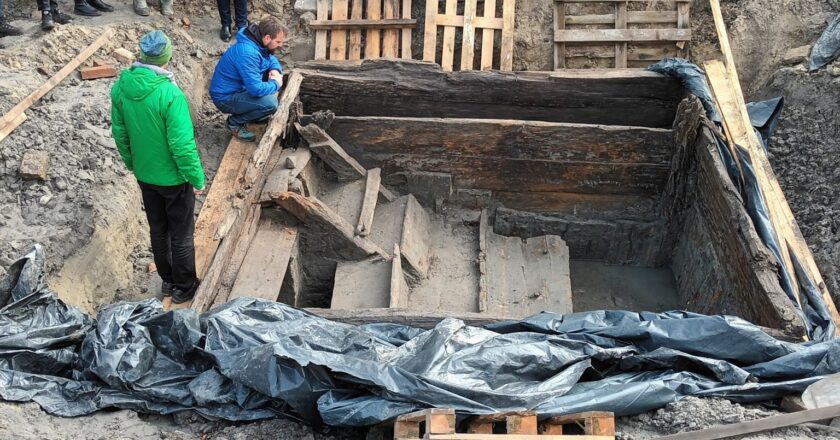 Zabytkowa mykwa (rytualna łaźnia żydowska) odkryta podczas prac archeologicznych w Oświęcimiu – widoczne schody i drewniane ściany wykonanego z bali zbiornika, wokół miejsce wykopalisk zabezpieczone folią budowlaną.