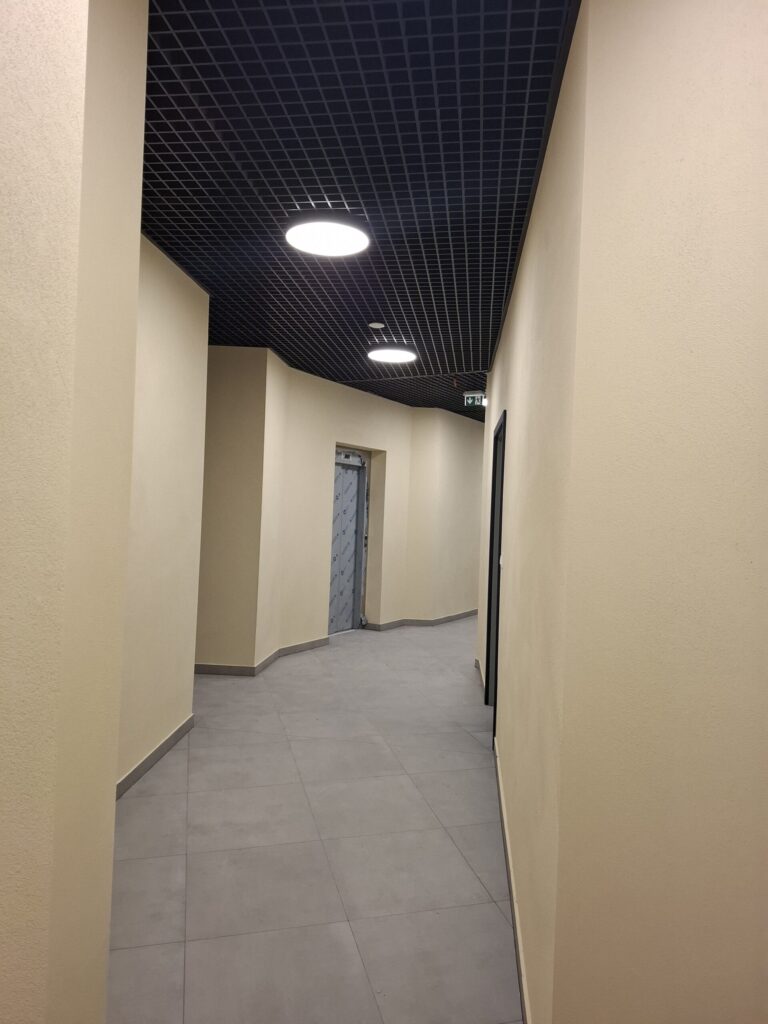 Odnowiona zabytkowa kamienica przy ul. Mickiewicza w Oświęcimiu, z elegancką jasną elewacją, zielonymi balkonami i drewnianymi oknami, w otoczeniu drzew i błękitnego nieba.