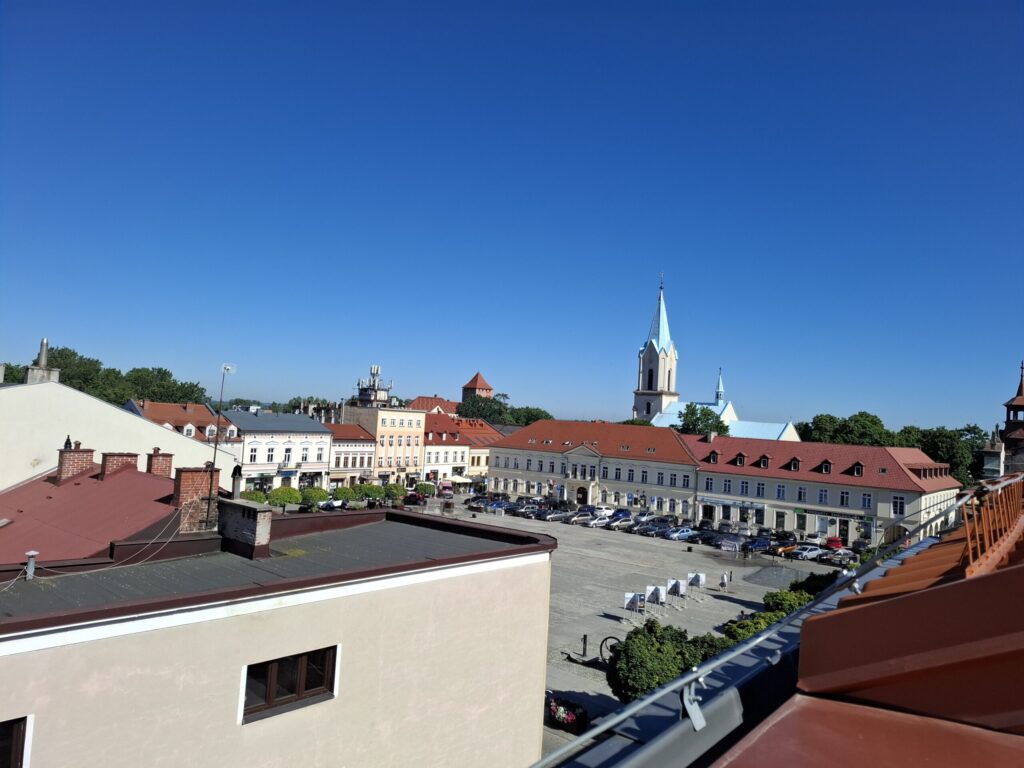 Odnowiona zabytkowa kamienica przy ul. Mickiewicza w Oświęcimiu, z elegancką jasną elewacją, zielonymi balkonami i drewnianymi oknami, w otoczeniu drzew i błękitnego nieba.