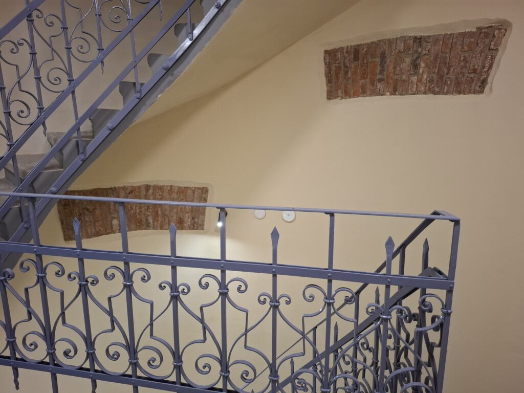 Odnowiona zabytkowa kamienica przy ul. Mickiewicza w Oświęcimiu, z elegancką jasną elewacją, zielonymi balkonami i drewnianymi oknami, w otoczeniu drzew i błękitnego nieba.
