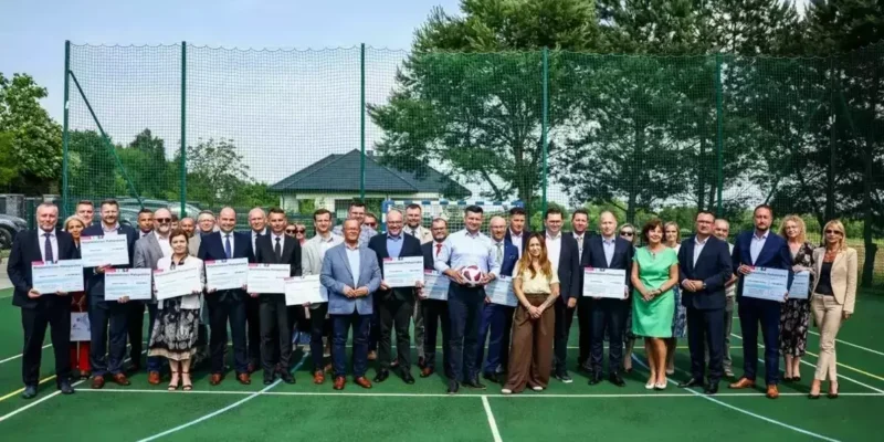 Przedstawiciele małopolskich samorządów z promesami Małopolskiego Programu Rozwoju Bazy Sportowej 2025, wręczonymi przez marszałka województwa na boisku. Kęty