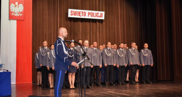 Funkcjonariusze Policji podczas uroczystości Święta Policji 2025 w Oświęcimskim Centrum Kultury – wręczanie awansów i odznaczeń przez komendanta, w tle sztandar Komendy Powiatowej Policji w Oświęcimiu.
