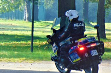Policjant z oświęcimskiej drogówki na służbowym motocyklu patroluje teren zielony w pełnym umundurowaniu i kasku ochronnym