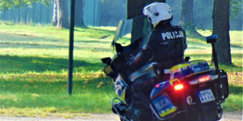 Policjant z oświęcimskiej drogówki na służbowym motocyklu patroluje teren zielony w pełnym umundurowaniu i kasku ochronnym