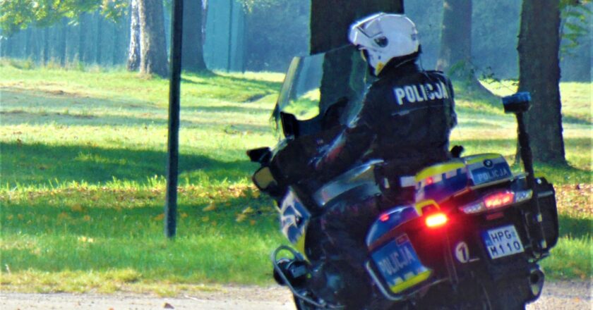 Policjant z oświęcimskiej drogówki na służbowym motocyklu patroluje teren zielony w pełnym umundurowaniu i kasku ochronnym
