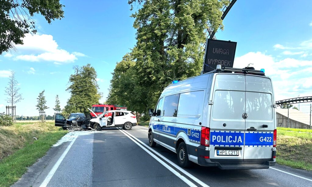 Służby ratunkowe na miejscu czołowego zderzenia dwóch samochodów osobowych na drodze krajowej nr 44 w Zatorze. Na pierwszym planie policyjny radiowóz i tablica z napisem „Uwaga wypadek”, w tle straż pożarna i rozbite pojazdy blokujące jezdnię.
