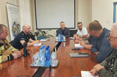 Posiedzenie Sztabu Kryzysowego Gminy Brzeszcze 28 lipca 2025 r. — przy stole obrad zasiadają przedstawiciele straży pożarnej, policji, urzędu gminy oraz innych służb. W tle baner promujący gminę Brzeszcze.