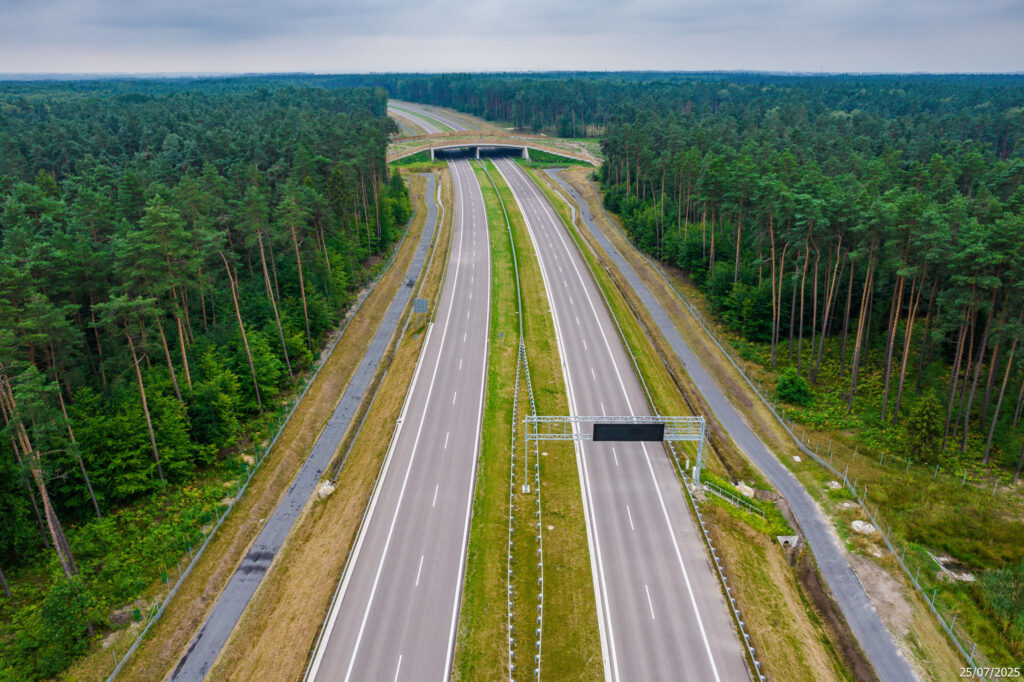 Nowo wybudowany węzeł drogowy na drodze ekspresowej S-1 w pobliżu Oświęcimia, widziany z lotu ptaka. Zdjęcie przedstawia skrzyżowanie wielopoziomowe z nowoczesnymi jezdniami, barierami energochłonnymi, ekranami akustycznymi i oznakowaniem kierunkowym. Otoczenie stanowią pola uprawne i lasy. Data wykonania zdjęcia: 25 lipca 2025 roku.