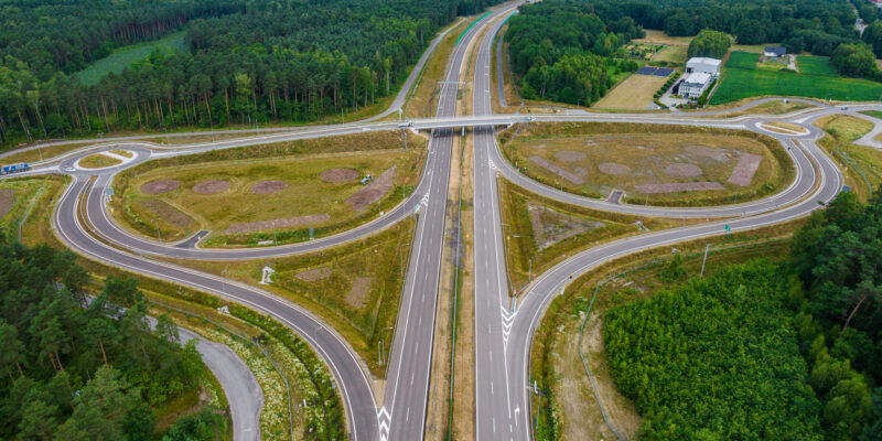 Węzeł drogowy Wola na budowanej trasie ekspresowej S1 między Kosztowami a Oświęcimiem. Zdjęcie lotnicze przedstawia nową infrastrukturę drogową otoczoną lasem i terenami wiejskimi. Widoczne są jezdnie, ronda, estakady oraz pasy włączeń i zjazdów. Data wykonania zdjęcia: 8 lipca 2025 roku.