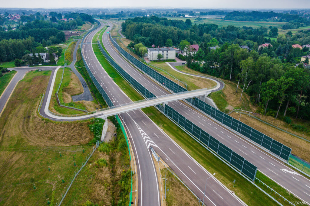 Nowo wybudowany węzeł drogowy na drodze ekspresowej S-1 w pobliżu Oświęcimia, widziany z lotu ptaka. Zdjęcie przedstawia skrzyżowanie wielopoziomowe z nowoczesnymi jezdniami, barierami energochłonnymi, ekranami akustycznymi i oznakowaniem kierunkowym. Otoczenie stanowią pola uprawne i lasy. Data wykonania zdjęcia: 25 lipca 2025 roku.