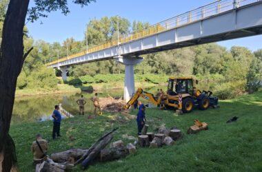 Strażacy i pracownicy Wód Polskich usuwają zator z koryta Soły pod kładką w Oświęcimiu przy pomocy koparki i lin.