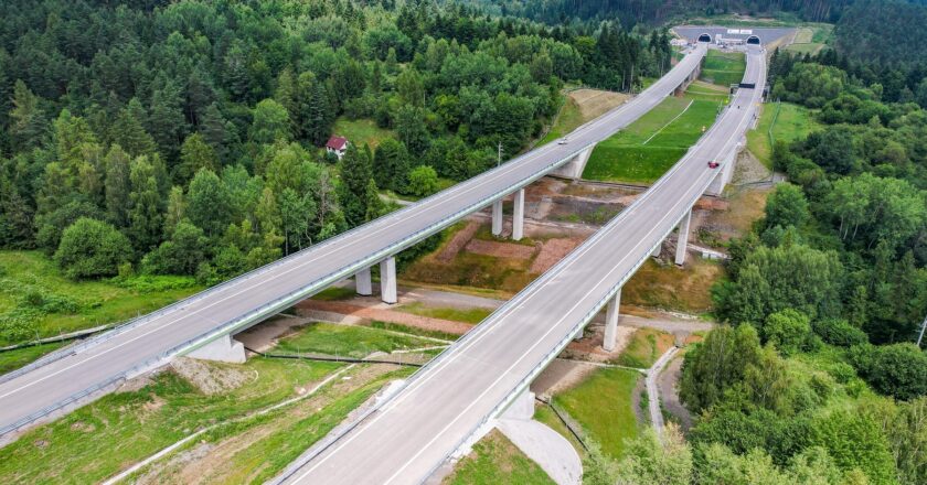 Widok z drona na imponującą estakadę drogi ekspresowej S1 w rejonie Węgierskiej Górki. Konstrukcja przebiega wysoko nad doliną, pośród gęstych lasów i zabudowań. Widoczne ekrany akustyczne i oznaczenia wykonawcy inwestycji – firmy Mirbud.