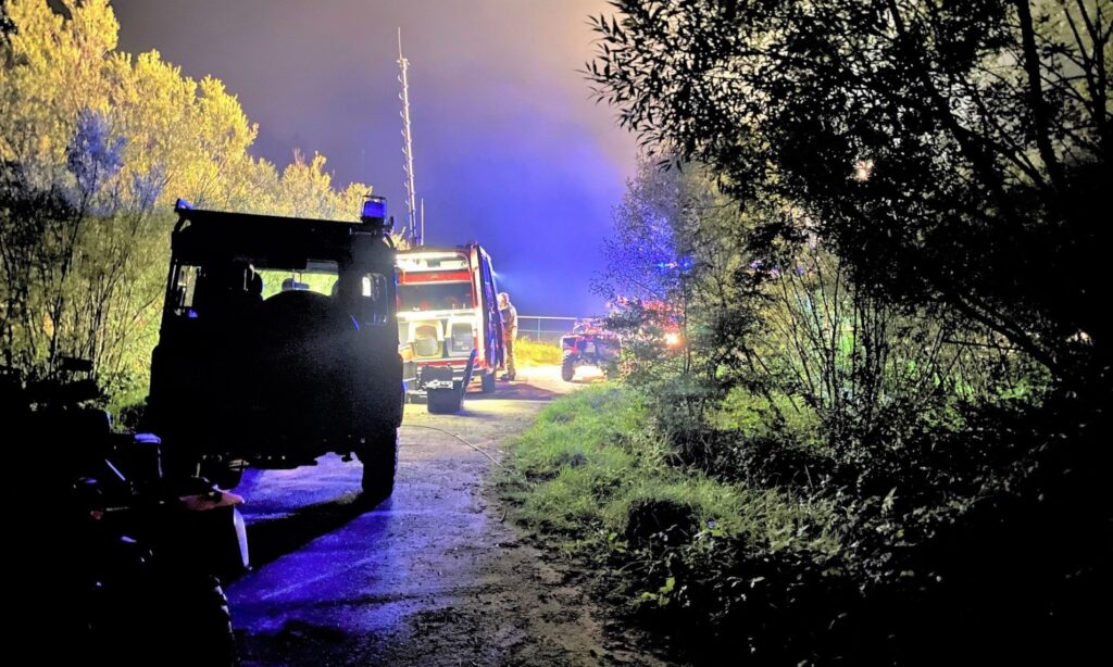 Nocna akcja poszukiwawczo-ratownicza w lesie w gminie Kęty. Na zdjęciu strażacy i policjanci przy pojazdach służbowych oświetlonych światłami akcji.