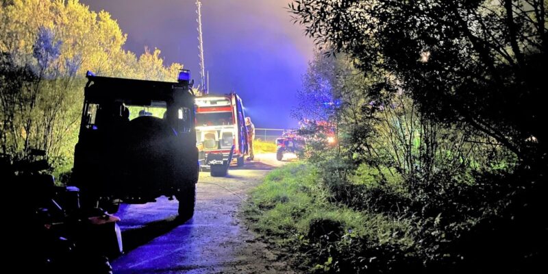 Nocna akcja poszukiwawczo-ratownicza w lesie w gminie Kęty. Na zdjęciu strażacy i policjanci przy pojazdach służbowych oświetlonych światłami akcji.
