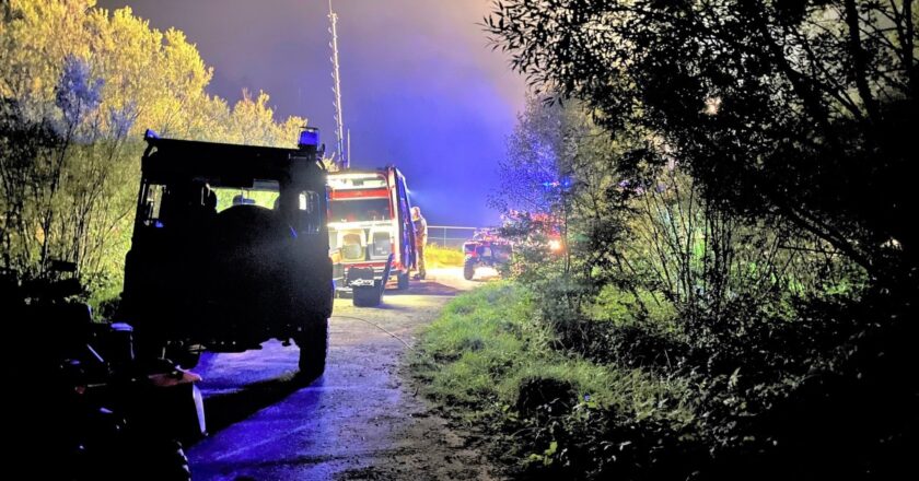 Nocna akcja poszukiwawczo-ratownicza w lesie w gminie Kęty. Na zdjęciu strażacy i policjanci przy pojazdach służbowych oświetlonych światłami akcji.
