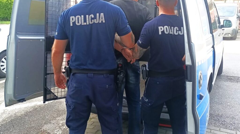 Policjanci z Oświęcimia prowadzą zatrzymanego mężczyznę w kajdankach do radiowozu.
