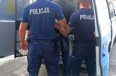 Policjanci z Oświęcimia prowadzą zatrzymanego mężczyznę w kajdankach do radiowozu.