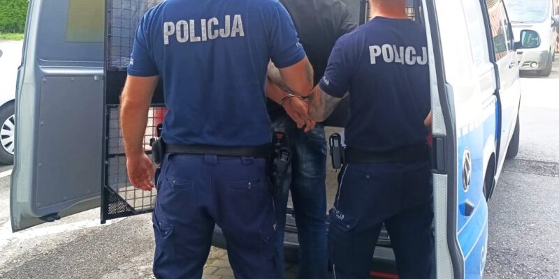Policjanci z Oświęcimia prowadzą zatrzymanego mężczyznę w kajdankach do radiowozu.