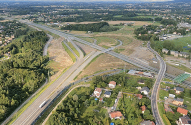 Widok z lotu ptaka na rozbudowywany węzeł drogowy w ciągu drogi ekspresowej S1 w Małopolsce, z widocznymi pasami ruchu, zjazdami, estakadami oraz otaczającą zabudową mieszkalną i terenami zielonymi.