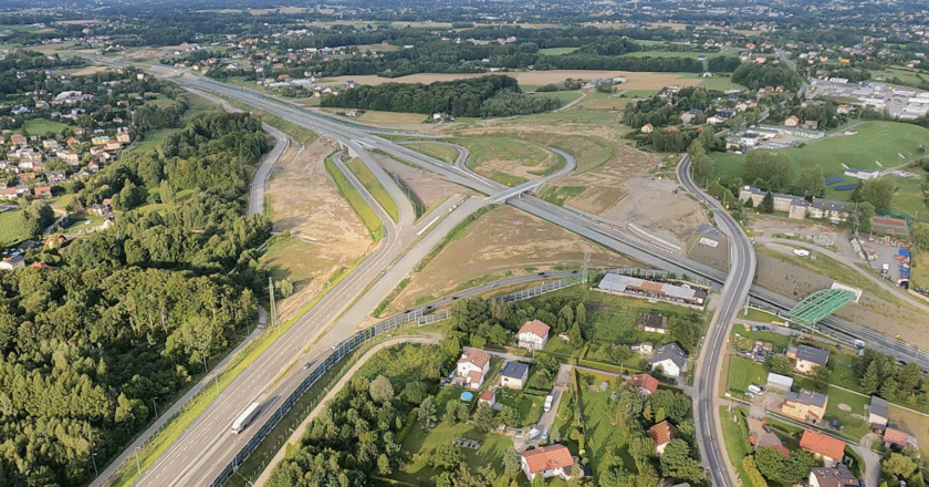 Widok z lotu ptaka na rozbudowywany węzeł drogowy w ciągu drogi ekspresowej S1 w Małopolsce, z widocznymi pasami ruchu, zjazdami, estakadami oraz otaczającą zabudową mieszkalną i terenami zielonymi.