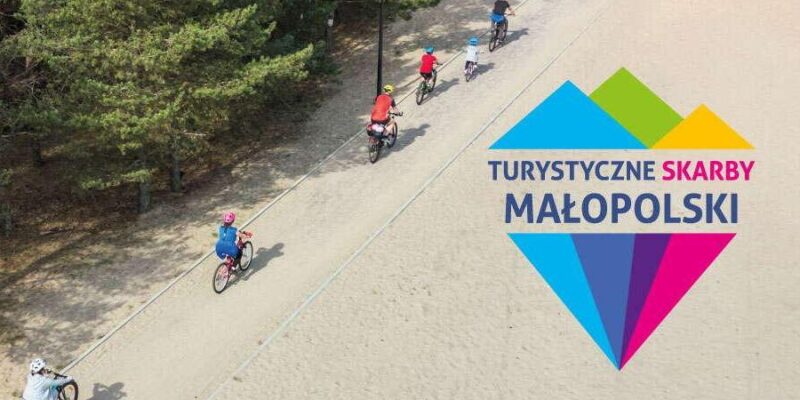 Grupa rowerzystów jadących ścieżką wśród drzew, logo konkursu Turystyczne Skarby Małopolski z kolorowym motywem gór.