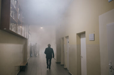 Zadymiony korytarz szkolny podczas próbnej ewakuacji w Trzebini, osoby opuszczają budynek zgodnie z procedurami bezpieczeństwa.