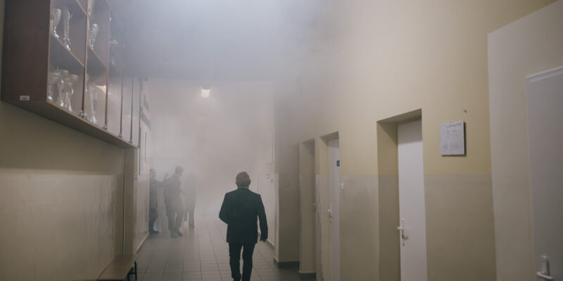 Zadymiony korytarz szkolny podczas próbnej ewakuacji w Trzebini, osoby opuszczają budynek zgodnie z procedurami bezpieczeństwa.