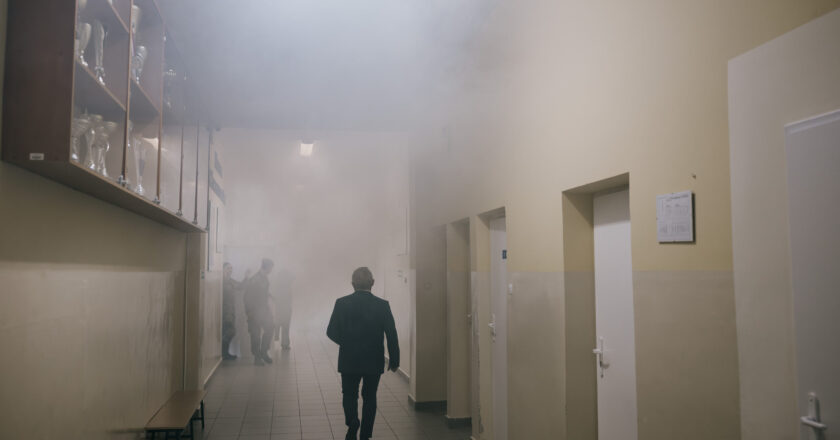 Zadymiony korytarz szkolny podczas próbnej ewakuacji w Trzebini, osoby opuszczają budynek zgodnie z procedurami bezpieczeństwa.