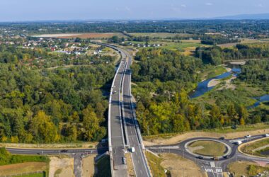 Widok z drona na nowo wybudowany odcinek południowej obwodnicy Oświęcimia – most nad rzeką Sołą i rondo turbinowe, otoczone zielenią i zabudową jednorodzinną. Trwa budowa drugiej nitki jezdni.
