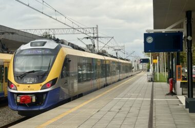 Pociąg Kolei Małopolskich stoi przy peronie na dworcu kolejowym w Oświęcimiu. W tle widać nowe ekrany informacyjne, zegar oraz zadaszenie peronu.
