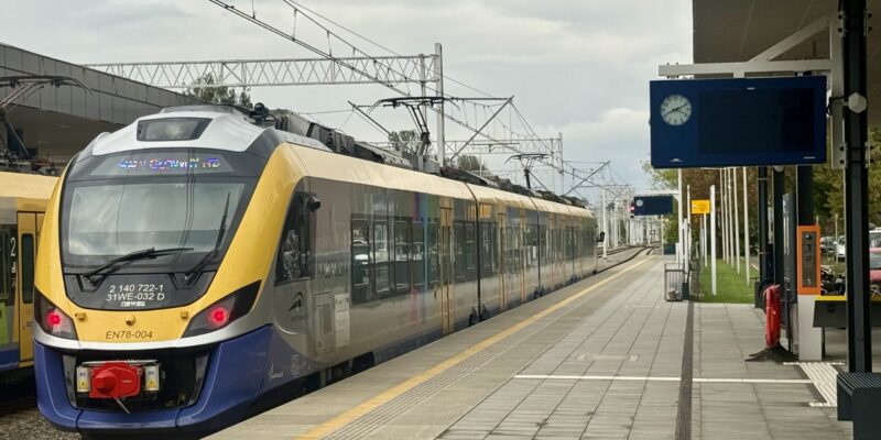Pociąg Kolei Małopolskich stoi przy peronie na dworcu kolejowym w Oświęcimiu. W tle widać nowe ekrany informacyjne, zegar oraz zadaszenie peronu.
