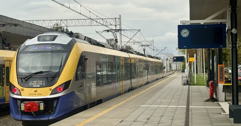 Pociąg Kolei Małopolskich stoi przy peronie na dworcu kolejowym w Oświęcimiu. W tle widać nowe ekrany informacyjne, zegar oraz zadaszenie peronu.