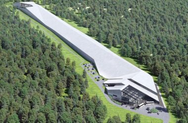 Wizualizacja nowoczesnej hali narciarskiej w Babicy w gminie Wadowice, otoczonej lasem. Długi, kryty stok o imponującej długości 650 metrów ciągnie się wśród drzew, prowadząc do przeszklonego budynku z parkingiem i autobusami przed wejściem.