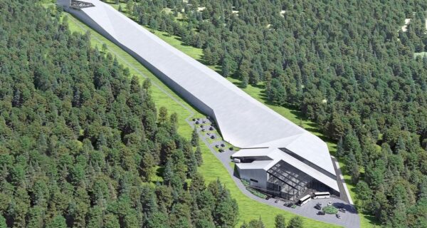 Wizualizacja nowoczesnej hali narciarskiej w Babicy w gminie Wadowice, otoczonej lasem. Długi, kryty stok o imponującej długości 650 metrów ciągnie się wśród drzew, prowadząc do przeszklonego budynku z parkingiem i autobusami przed wejściem.