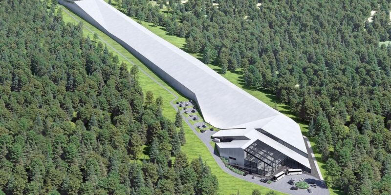 Wizualizacja nowoczesnej hali narciarskiej w Babicy w gminie Wadowice, otoczonej lasem. Długi, kryty stok o imponującej długości 650 metrów ciągnie się wśród drzew, prowadząc do przeszklonego budynku z parkingiem i autobusami przed wejściem.