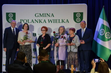 Uhonorowane mieszkanki Polanki Wielkiej podczas obchodów 700-lecia gminy. Kobiety trzymają róże i medale, stojąc obok władz samorządowych na tle ścianki z napisem „Gmina Polanka Wielka”.