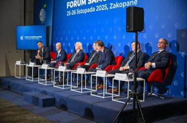 Paneliści siedzący na scenie podczas Forum Samorządowego w Zakopanem; w tle niebieska ściana z logo wydarzenia i datą „25–26 listopada 2025”, Radosław Włoszek po lewej zabiera głos do mikrofonu.