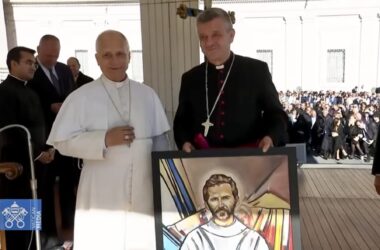 Biskup Roman Pindel przekazuje papieżowi Leonowi XIV obraz z wizerunkiem bł. Michała Tomaszka podczas audiencji na Placu św. Piotra; obaj stoją obok siebie na podium, w tle widać uczestników audiencji.