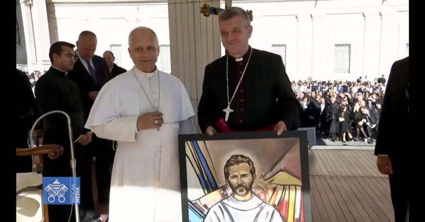 Biskup Roman Pindel przekazuje papieżowi Leonowi XIV obraz z wizerunkiem bł. Michała Tomaszka podczas audiencji na Placu św. Piotra; obaj stoją obok siebie na podium, w tle widać uczestników audiencji.