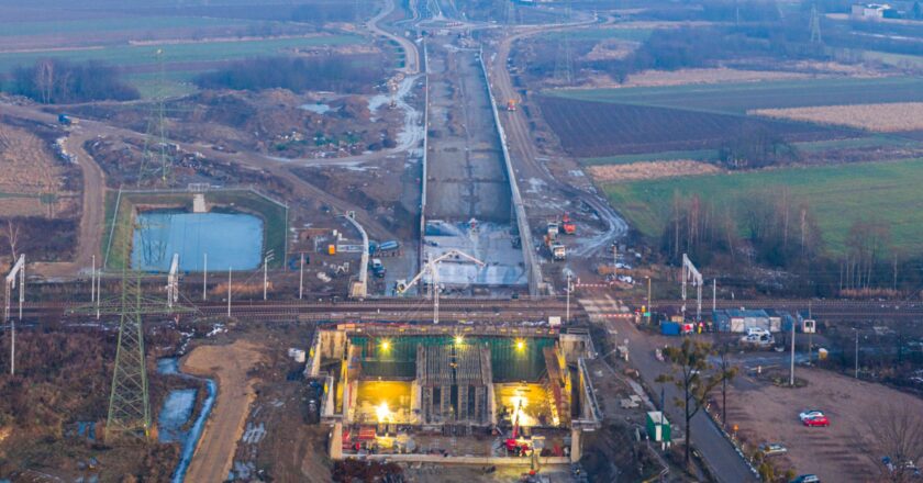 Widok z drona na budowę obwodnicy Oświęcimia: powstający tunel pod torami kolejowymi oraz długi odcinek nowej drogi przebiegającej przez tereny rolnicze w rejonie Brzezinki.