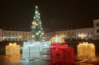 Świąteczna iluminacja na Rynku Głównym w Oświęcimiu: wysoka choinka, świetlne prezenty oraz dekoracyjna fontanna otoczone miejskimi kamienicami w wieczornej scenerii.