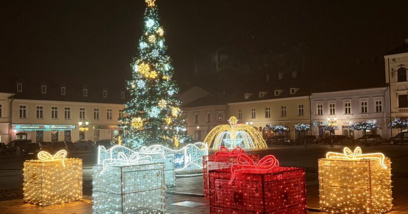 Świąteczna iluminacja na Rynku Głównym w Oświęcimiu: wysoka choinka, świetlne prezenty oraz dekoracyjna fontanna otoczone miejskimi kamienicami w wieczornej scenerii.