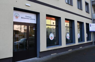 Wejście do Centrum Aktywności Lokalnej w Oświęcimiu – elewacja budynku z przeszklonymi drzwiami i oknami oznaczonymi logo Centrum Usług Społecznych.