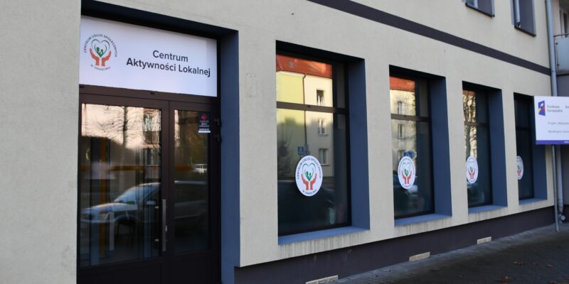 Wejście do Centrum Aktywności Lokalnej w Oświęcimiu – elewacja budynku z przeszklonymi drzwiami i oknami oznaczonymi logo Centrum Usług Społecznych.